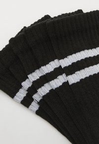 Schwarze Socken mit zwei horizontalen weißen Streifen, aus geripptem Strickmaterial, mit einer weichen Textur und einem klassischen Design.