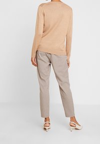 Beige Strickpullover mit langen Ärmeln, kombiniert mit braunen karierten Hosen. Das Outfit hat eine lockere Passform und eine weiche Textur.