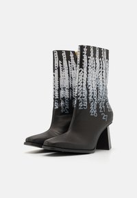 Botines negros con textura brillante, con números gráficos blancos superpuestos. Puntera cuadrada y un tacón geométrico ancho. Detalle de cremallera dorada.