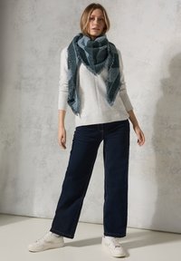 Blå og grå ternet uldsvale med frynser; båret over en lys strikket trøje og parret med bredbenede mørke jeans og hvide sneakers.