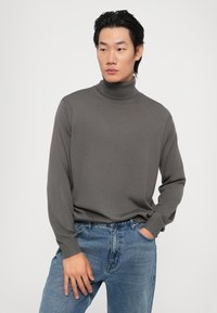 Pulover gri cu guler înalt, fabricat dintr-un material tricotat moale, având mâneci lungi și un design ajustat, asortat cu blugi albaștri deschiși.