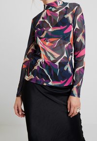 Långärmad, mångfärgad topp med hög hals, abstrakta bladmönster i lila, orange, grön och svart, tillverkad av genomskinligt material.