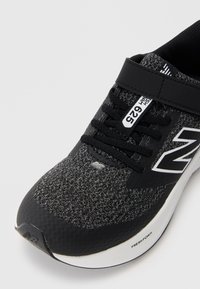 Chaussure de sport noire avec une tige en tricot texturé, des accents synthétiques, un système de laçage, et une semelle intermédiaire blanche portant l'étiquette "FRESH FOAM."
