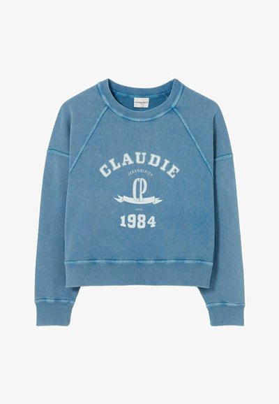 Sudadera azul con mangas raglán, que presenta un texto gráfico en blanco que dice “CLAUDIE SERENDIPITY CP 1984.” Material de algodón suave y texturizado.