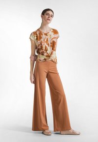 Bluzka w kwiatowy wzór w kolorze pomarańczowym i kremowym, związana w talii. Szerokie spodnie w kolorze terakoty. Całość uzupełniają beżowe baleriny.