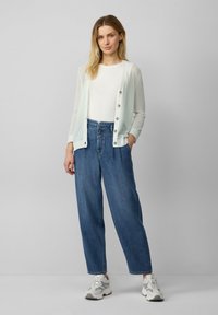 Hellgrüner Cardigan mit strukturierter Musterung und Knöpfen, kombiniert mit lockeren blauen Denim-Jeans und grauen Sneakers.