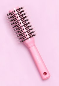 Brosse à cheveux ronde rose avec des poils aux pointes noires, un manche lisse et un trou pour accrocher. Le design est simple et fonctionnel.