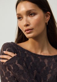 Krajkový top v tmavé barvě s květinovými vzory, dlouhými rukávy a širokým výstřihem. Hladká textura s viditelnými šicími detaily.