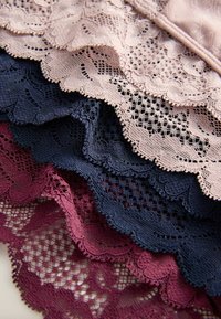 Zarter Spitzenstoff in Rosa, Marineblau und Burgunderrot, mit kunstvollen Blumenmustern und gewellten Rändern, schichtweise übereinander gelegt.