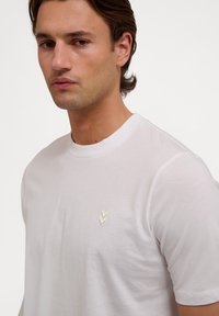 Hvid kortærmet t-shirt i blød bomuld med et lille beige broderet logo på brystet, rund halsudskæring og klassisk pasform.