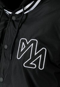 Black jacket featuring a white embroidered logo on the front, with a high collar and contrasting striped accents on the hood.