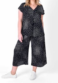 Czarna bluzka w groszki z dekoltem w serek i rękawami typu cap, zestawiona z szerokimi spodniami w groszki, dopełniona białymi trampkami.