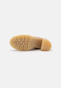 Suela de zapato de goma de color beige, con un dibujo en relieve que presenta líneas elevadas y un tacón redondeado. Textura suave en general.