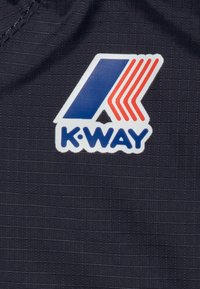 Logo K-Way in bianco e blu con strisce rosse su uno sfondo scuro e testurizzato. Il logo presenta una lettera 'K' stilizzata con accenti geometrici.