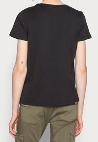 Svart bomullst-shirt med korta ärmar och rund halsringning, med en rak fåll och minimalistisk design. Bärs med olivgröna byxor.