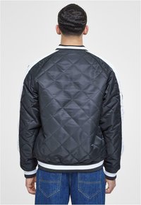 Quilted black bomber jacket with contrasting white side panels, ribbed cuffs, and waistband, featuring a smooth shiny texture.