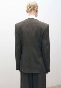 Blazer su misura grigio scuro con spalle strutturate e colletto bianco, visto da dietro, che mette in evidenza linee pulite e una trama liscia.
