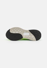 Semelle en caoutchouc noire et grise avec un motif texturé et des accents blancs. Présente un logo visible dans le midsole et une forme lisse et courbée.
