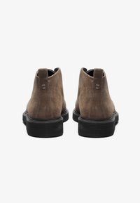 Botas de tobillo de ante marrón con tacón bajo, que cuentan con una suela de goma negra y detalles de costura, vistas desde la parte trasera.