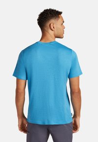 T-shirt a maniche corte, collo rotondo, di un vivace blu, realizzato in tessuto leggero con una superficie liscia. La vista posteriore mette in evidenza le cuciture pulite.