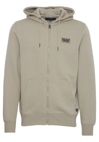 Sudadera con cremallera color beige hecha de una suave mezcla de algodón, que cuenta con un bolsillo frontal tipo canguro, capucha con cordón y un pequeño parche de logo en el pecho.