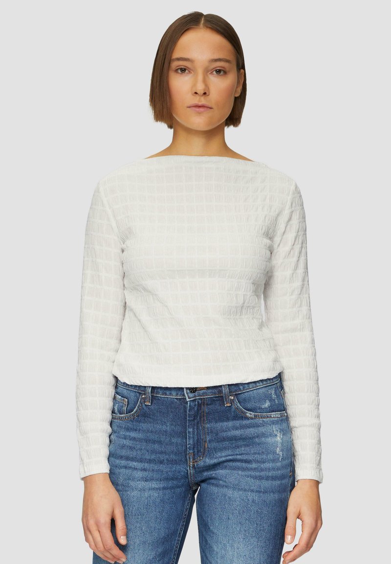 Haut blanc texturé à manches longues avec un décolleté carré, associé à un jean en denim bleu avec un léger effet délavé et des poches avant.