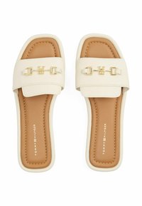 Chanclas de crema con una tira ancha que presenta herrajes dorados, plantilla beige y suela blanca. Material texturizado con costuras sutiles.