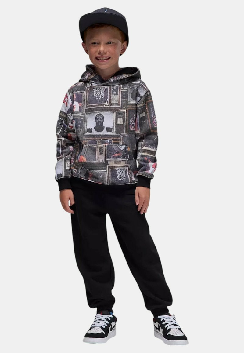 Felpa con cappuccio caratterizzata da un collage di schermi TV vintage e grafiche sportive, abbinata a pantaloni jogger neri e sneaker bianche.