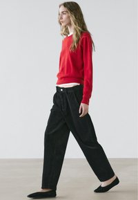 Pull rouge en tricot, pantalon noir ample et chaussures plates noires. Design simple, silhouette décontractée et style minimaliste.