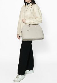 Borsa a mano in pelle beige, di forma rotonda, con manici doppi e chiusura con zip. Superficie texture e accessori in metallo. Design minimalista.