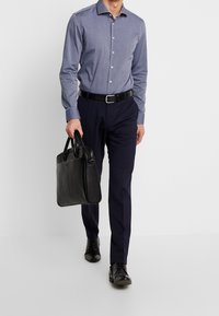 Niebieska koszula z długim rękawem, granatowe spodnie, czarny pasek i czarna skórzana teczka. Całość dopełniają eleganckie buty. Prosty krój z guzikami.