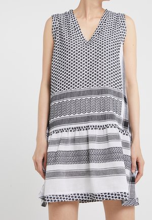 Mouwloze jurk met zwart-witte geometrische en gestreepte patronen, V-hals, losse pasvorm, gedragen door een staand persoon met ontspannen armen.