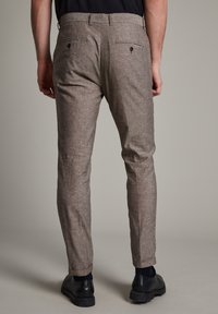 Bruna rutiga byxor med skräddarsydd passform, med två bakfickor och en mjuk textur, tillsammans med svarta skor.