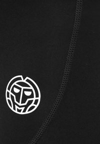 La tela atlética negra presenta una textura suave con un logotipo circular blanco que muestra una cara estilizada. Costura en contraste en los bordes.