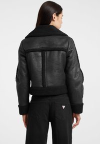 Giacca in shearling nera con colletto ampio, finitura testurizzata e dettagli in peluche a contrasto. Presenta un retro strutturato e un design cropped.