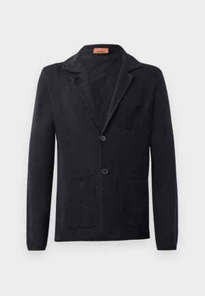 Blazer de punto negro con un patrón de espiga, solapa de muesca, dos bolsillos frontales y dos botones. Etiqueta visible en el interior del cuello.