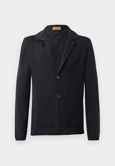 Fekete kötött blézer herringbone mintával, csúcsos nyakkal, két elülső zsebbel és két gombbal. Címke látható a gallér belső oldalán.