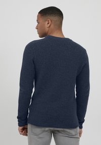 Mørkeblå genser med lange ermer og teksturert strikkemønster, rund halslinning og tettsittende ermer, sett fra baksiden.