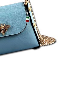Lichtblauwe leren handtas met gouden kettingriem, voorzien van bijenembleem en Italiaanse vlag charm, ritsluiting en een gestructureerde afwerking.