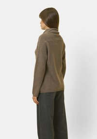 Brauner Strickpullover mit hohem Kragen, gerippten Bündchen und entspannter Passform. Glatte Textur und dezentes Steppdetail auf der Rückseite.