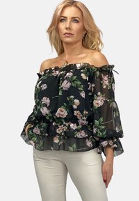 Czarna bluzka bez ramiączek z kwiecistym wzorem, przezroczysty materiał, falbaniasty dekolt, dzwoniaste rękawy i marszczona talia. Stylizowana z jasnymi spodniami.