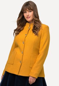 Cappotto in misto lana giallo con una vestibilità strutturata, scollatura arrotondata, chiusura con bottoni e due tasche anteriori. Texture morbida e design su misura.
