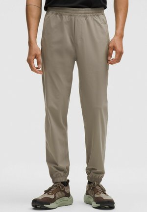 Lätta beige joggerbyxor med elastisk midja. Har en jämn yta, anklaffar och sidofickor, ihop med bruna sneakers.