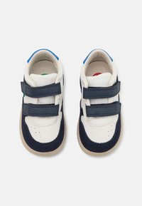 Baskets blanches et marine avec deux brides Velcro, une tige en toile douce, un bout perforé et des semelles en caoutchouc texturé. Des accents bleus et verts sont inclus.