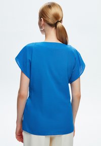 Top blu con maniche corte, dal taglio rilassato, texture liscia e scollatura rotonda. Senza motivi o decorazioni, design semplice.