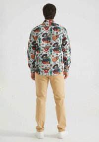 Chemise à manches longues avec boutonnières présentant un motif coloré inspiré du Mexique sur un fond bleu clair, fabriquée en tissu léger avec un col classique.