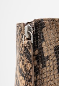Acercamiento a una cremallera de patrón de piel de serpiente marrón y negra en una bota de cuero con costuras detalladas.