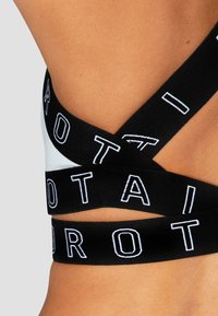 Bralette negra con tirantes entrecruzados que presentan letras blancas. Fabricado con un tejido suave y de textura lisa, destacando un diseño atlético.