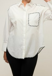 Weißes Hemd mit schwarzen gestreiften Akzenten an den Schultern und der Brusttasche, mit abgerundetem Saum und entspannter Passform. Baumwollmischmaterial.