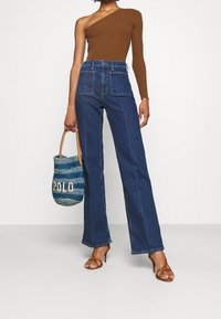 Hnědý žebrovaný top na jedno rameno, tmavě modré široké kalhoty s vysokým pasem a tkaná modrá kabelka s nápisem "POLO". Hnědé sandály na podpatku.